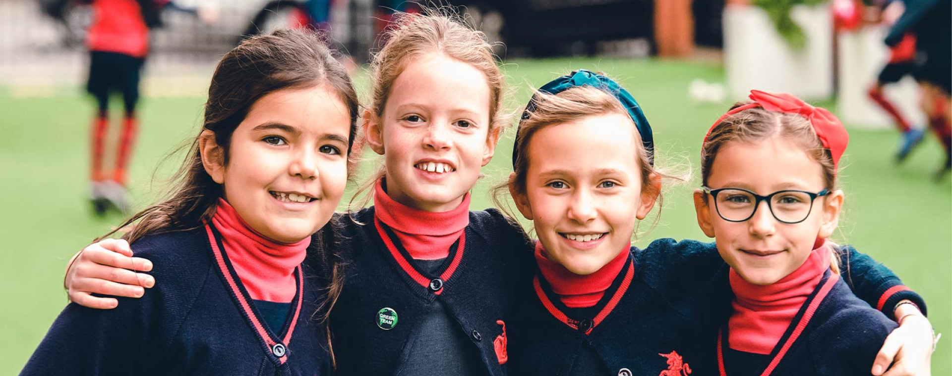 Four schoolgirls in navy Thomas's uniforms smiling together on a sports field