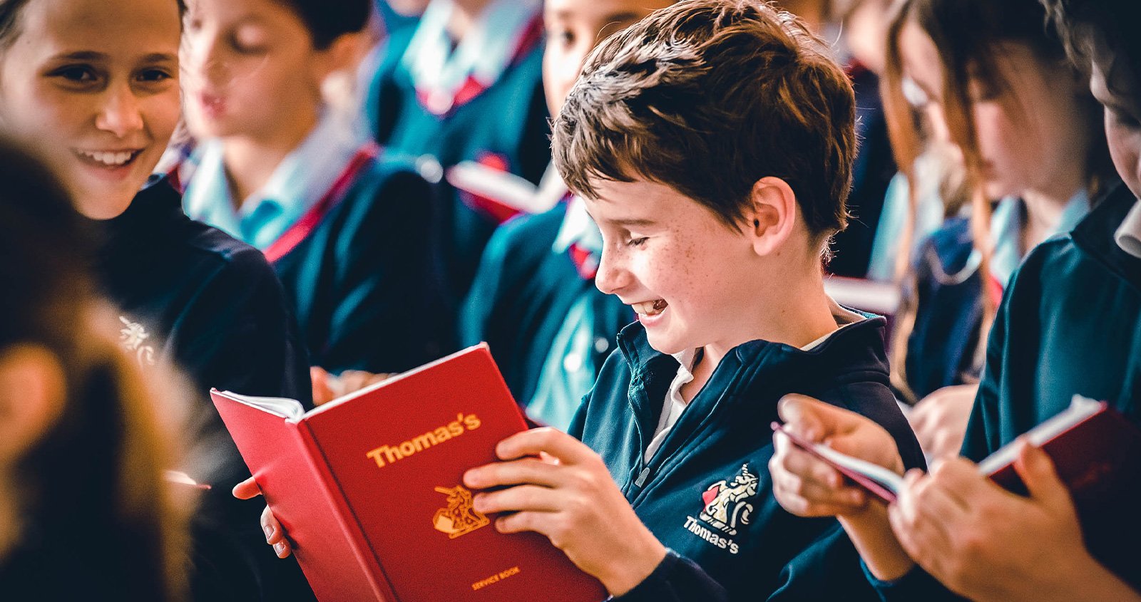 Schoolchildren in navy uniforms reading, one boy holding an open red Thomas's book