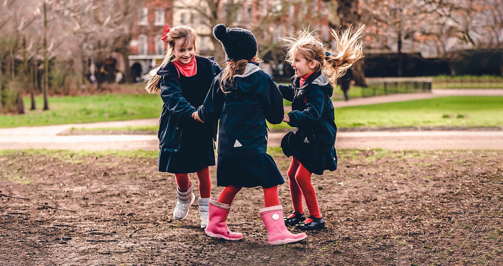 Three young children in navy coats walking together in a park — TomCom case study
